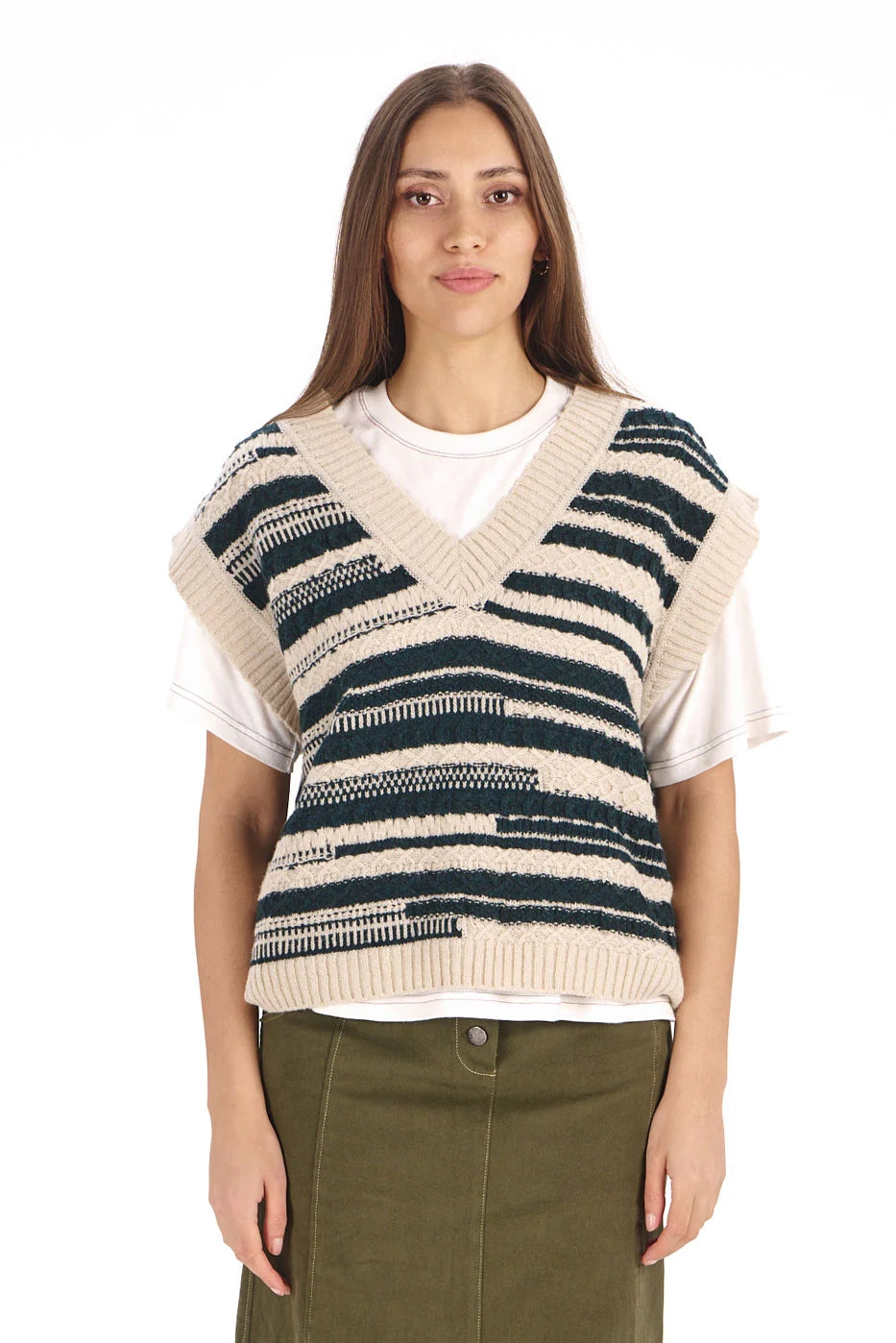 A woman modeling a sleeveless knit V-neck sweater vest with horizontal navy and beige stripes, layered over a white t-shirt and paired with an olive green skirt, against a plain white background.