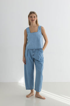 Woman wearing a light blue sleeveless top and pants on a white background