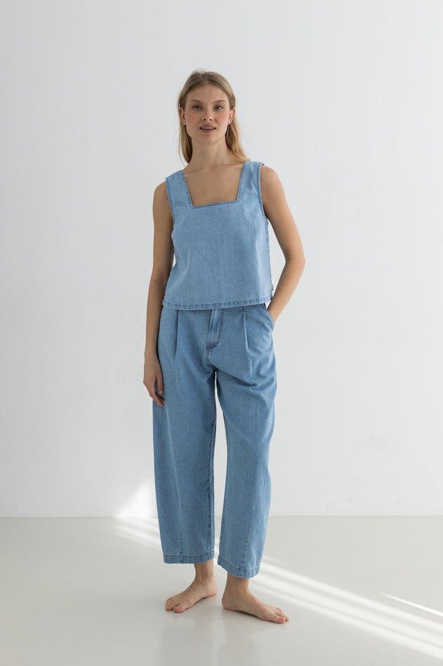 Woman wearing a light blue sleeveless top and pants on a white background
