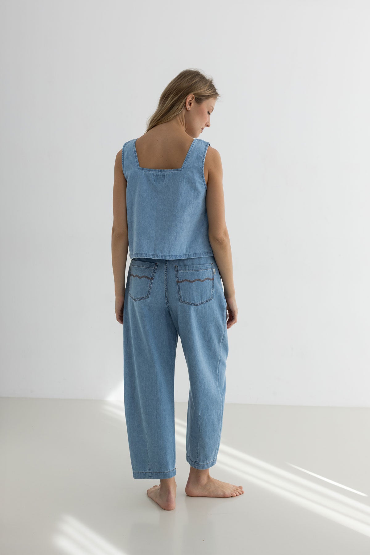 Woman wearing a light blue denim outfit standing on a white floor with a white wall background
