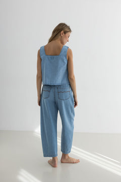 Woman wearing a light blue denim outfit standing on a white floor with a white wall background