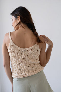Woman wearing a beige crochet tank top against a plain background
