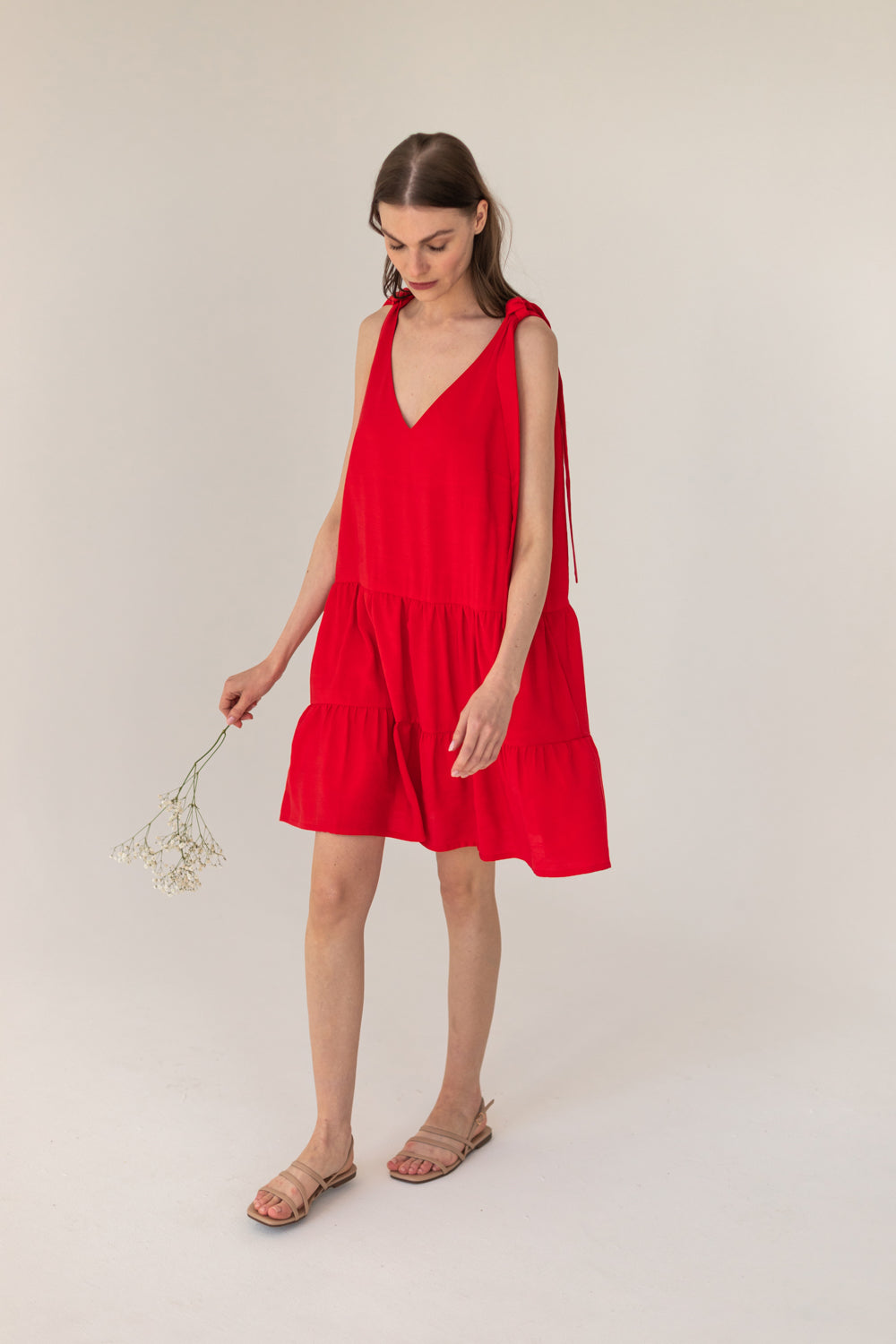 Woman wearing a red dress holding a small plant against a plain background