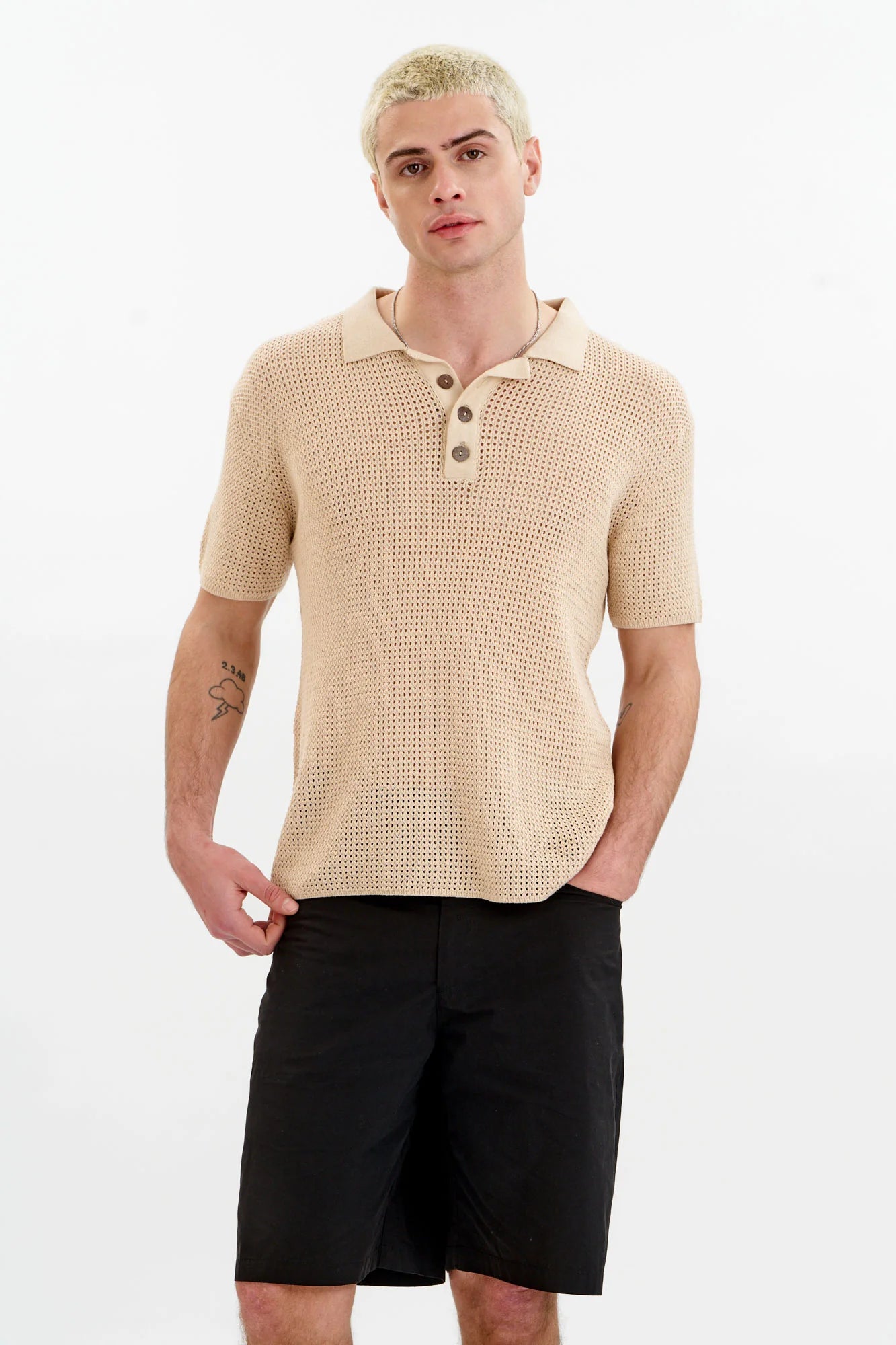 Man wearing a beige textured polo shirt and black shorts on a white background
