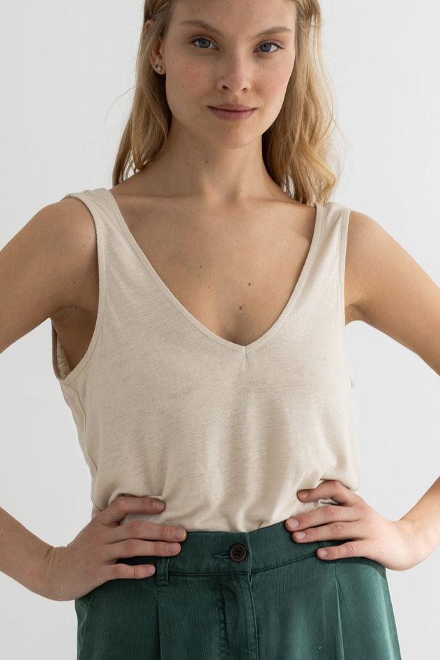 Woman wearing a beige tank top and green pants against a plain background
