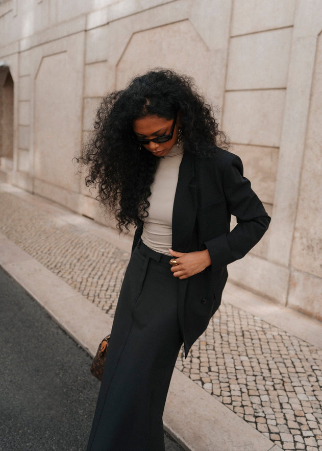 Woman in black blazer and pants walking on a street.