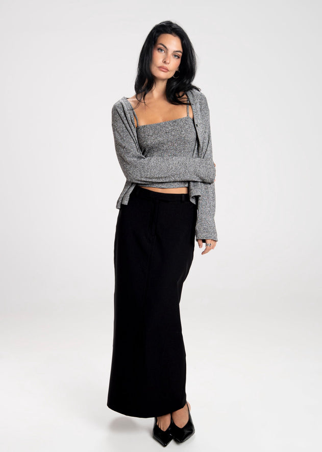 Woman wearing a gray cardigan over a black top and long black skirt on a white background