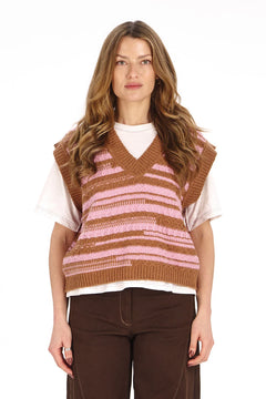 A woman modeling a brown and pink striped knit sweater vest over a white t-shirt and dark brown pants, shot against a solid white background.